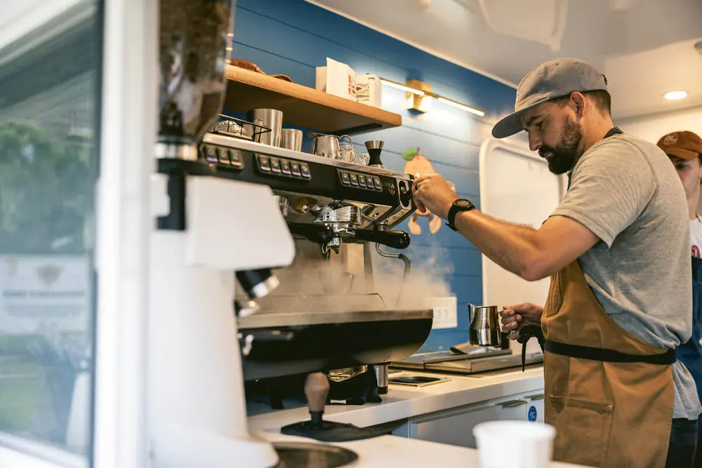 Barista steaming milk inside the Good Fruit coffee camper at Bearss Groves Tampa
