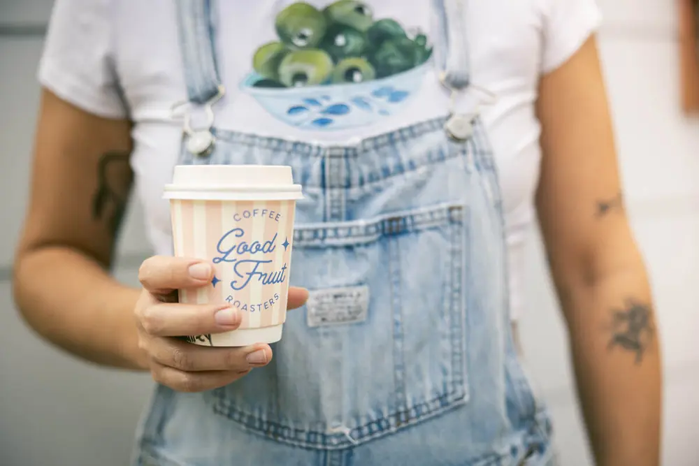 Customer in overalls holding a peach striped Good Fruit cup