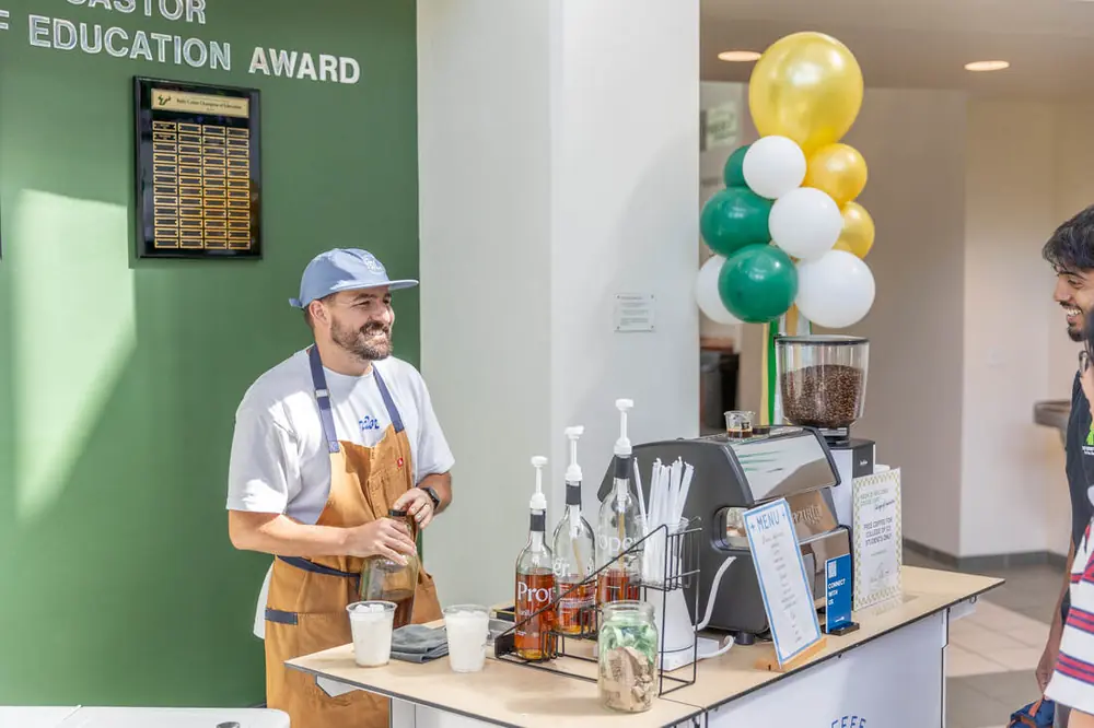Barista serving iced lattes from the Good Fruit coffee cart at a university event