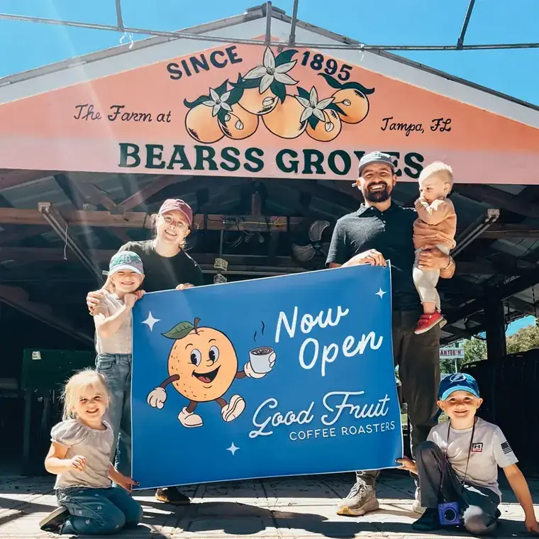 The Good Fruit family holding a Now Open banner under the historic Bearss Groves sign in Tampa