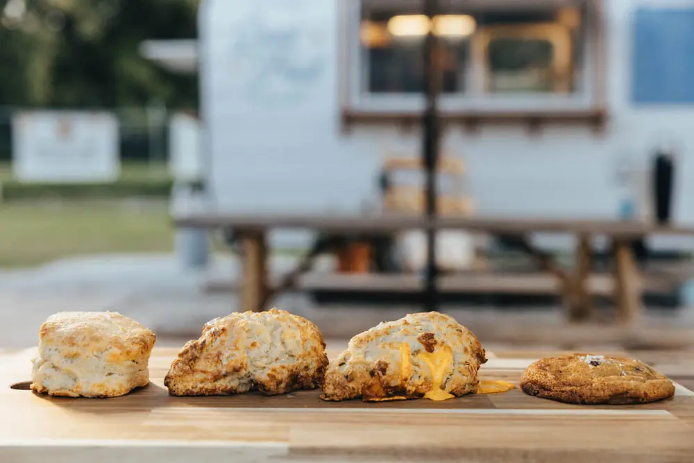 Bakery case lineup — buttermilk biscuit, glazed scone, cheddar scone, and sea-salt chocolate chip cookie in front of the Good Fruit camper