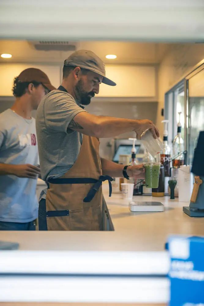 Barista pouring oat milk into an iced matcha inside the Good Fruit camper