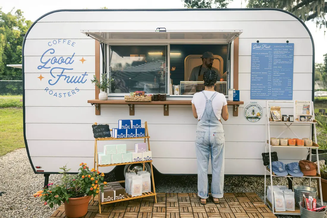 A customer ordering at the Good Fruit camper window at Bearss Groves, with the menu board, Valor beans, and merch shelves